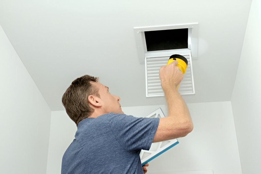 Technician using a flashlight to inspect a ceiling air vent for duct cleaning in Rochester NY, ensuring efficient airflow and better indoor air quality.